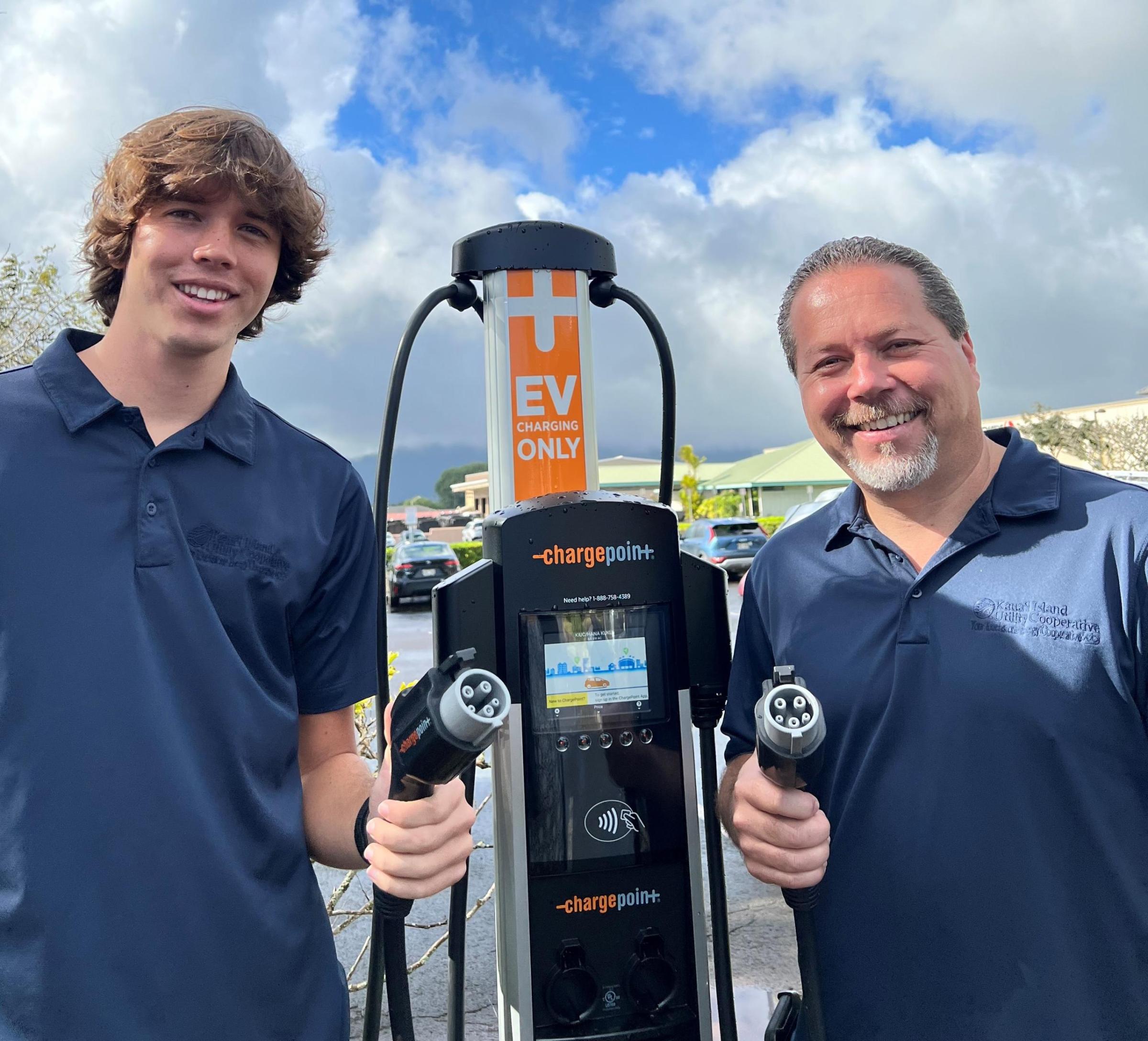 two men smiling outside holding EV chargers