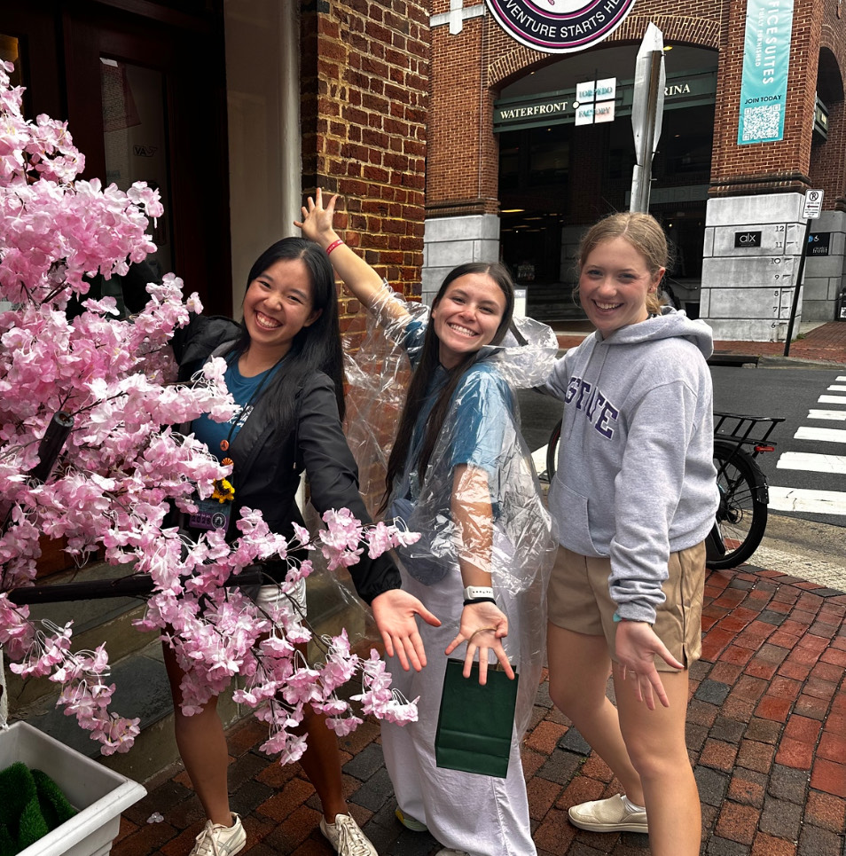 Three teenage girls standing and smiling by a flowering pink tree
